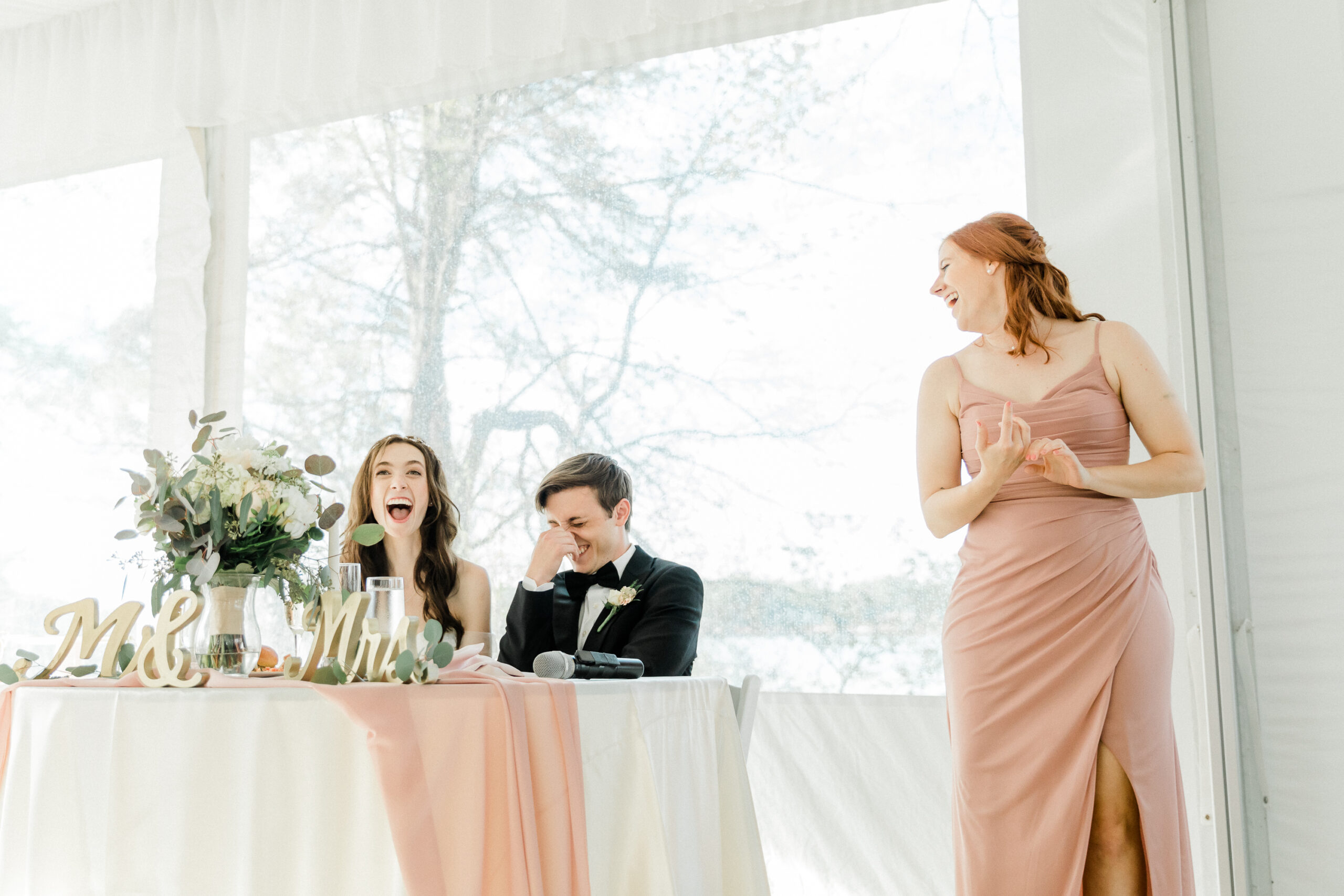 A bride and groom burst out in laughter while the maid of honor gives a speech in an Annapolis, Maryland.